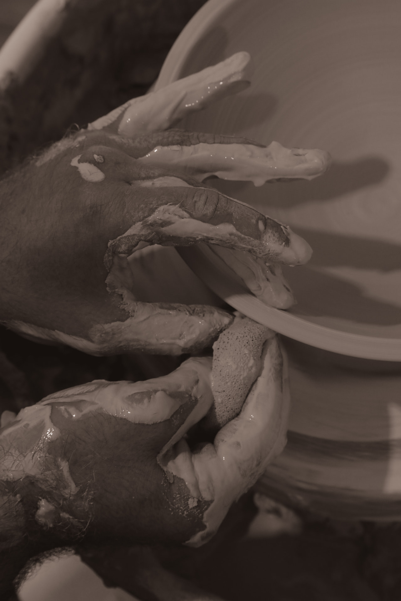 Two clay-covered hands shaping the rim of a spinning bowl