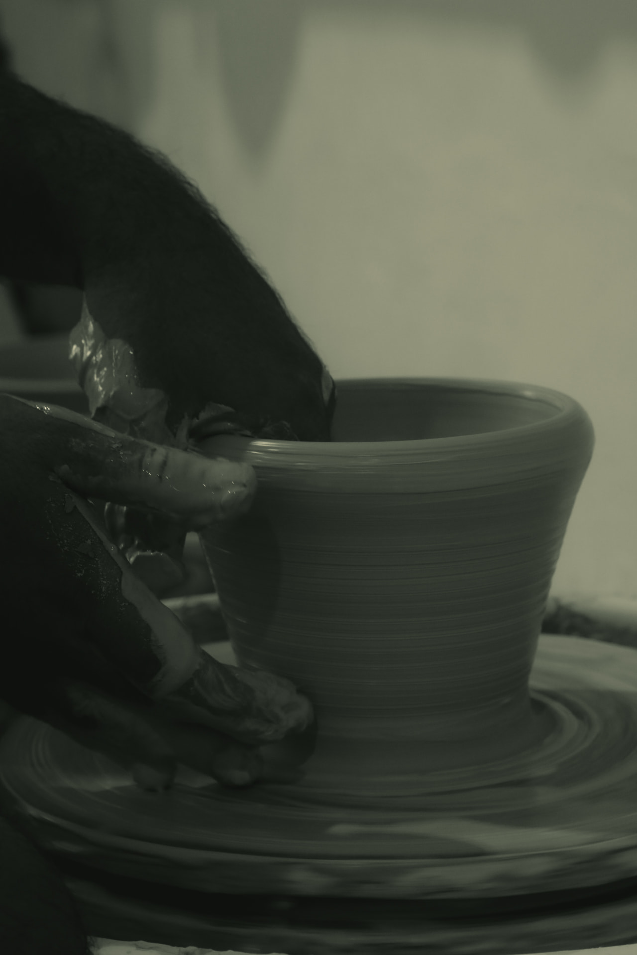 Hands drawing up the wall of a cup on the wheel
